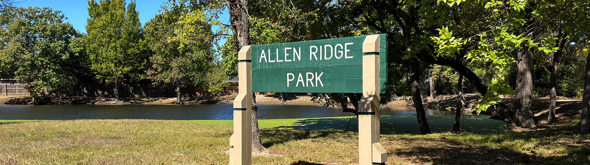 Allen Ridge Park sign in front of a pond, surrounded by trees.