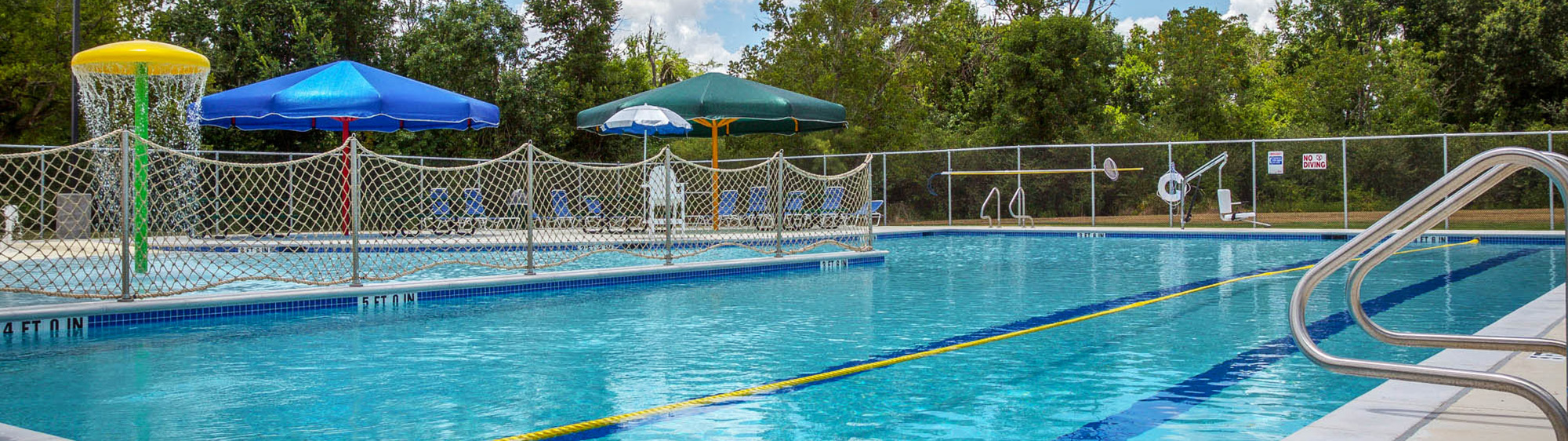 Photo of blue water at Sadie Thomas Pool with splash park elements sprinkling water on pavement